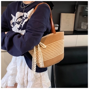 Detailed close-up of woven straw tote bag featuring white lace bow and leather shoulder strap