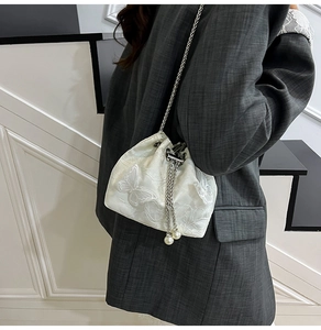 Detail of white drawstring bucket bag featuring 3D butterfly embroidery and pearl charms