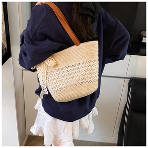 Detail of woven straw tote bag featuring a lace bow and brown leather handles