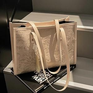 Chic beige tote bag with floral embossing and tassel detail on urban lifestyle background