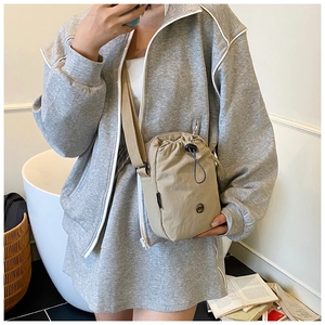 Model wearing a khaki nylon crossbody bag with drawstring closure in a cozy home setting