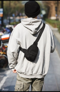 Rear view of a black waterproof nylon crossbody bag worn over a grey street style hoodie