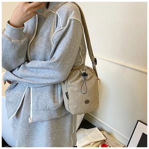 Adjustable beige nylon crossbody bag with drawstring closure shown on a female model