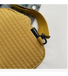 Close-up of yellow checkered canvas crossbody bag with brand label and woven strap details