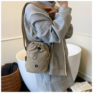 Detailed close-up of khaki nylon drawstring crossbody bag worn by a model in casual setting