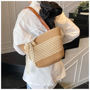 Close-up of striped straw tote bag featuring white lace bow and brown leather strap