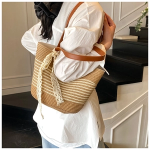 Detail of striped woven straw tote bag featuring brown leather straps and lace ribbon trim