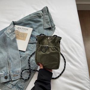 Detail of army green nylon mini crossbody bag with drawstring and woven strap on white bedding