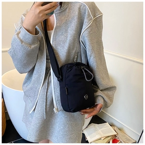 Detail of waterproof nylon crossbody bag featuring drawstring closure and metal ring accents