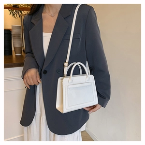 Sac à main en cuir blanc avec bandoulière porté avec un blazer gris et une robe blanche
