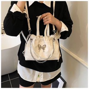Detail of cream fabric handbag featuring silver butterfly and pearl chain accessories
