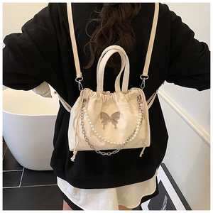 Detail of cream mini backpack with silver butterfly charm and pearl chain decoration
