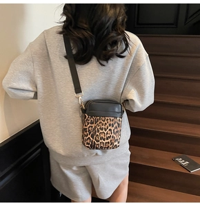 Detail of crossbody bag with leopard print base and black leather top on wide strap