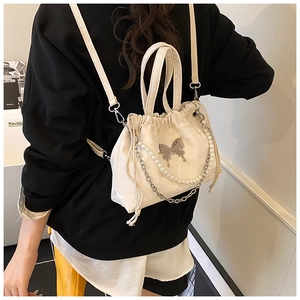 Detail of cream canvas drawstring backpack with pearl chain and metal bow decoration
