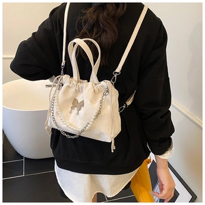 Detail of white drawstring backpack featuring metallic butterfly and pearl chain ornaments