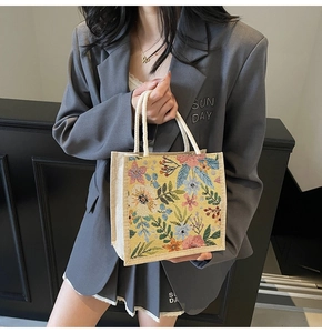 Detailaufnahme der Blumenstickerei auf Leinen-Lunchtasche mit weißen Griffen an einem Model