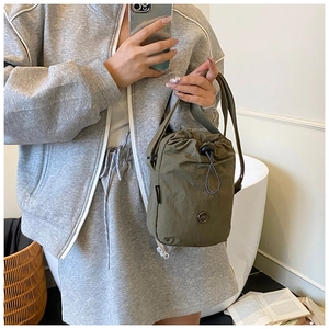 Olive green nylon bucket bag with drawstring closure and metal logo shown in a lifestyle mirror selfie