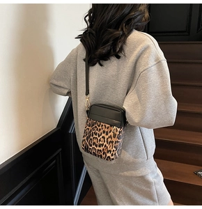Detail of leopard print canvas and black leather crossbody bag with golden metal hardware