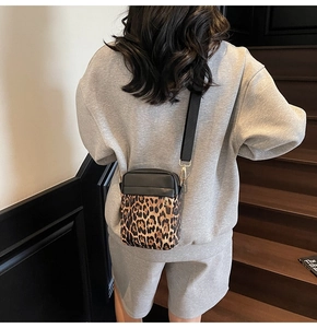 Detailed view of mixed black leather and leopard print cross-body bag with gold hardware