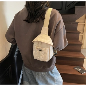 Detail of a beige quilted crossbody bag with adjustable wide strap shown on a model