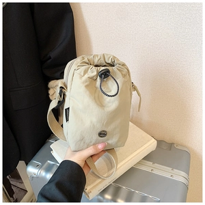 Detail of light khaki nylon crossbody bag with drawstring closure and metal badge