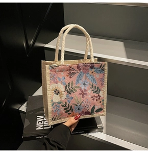 Detail der floralen Leinen-Lunch-Tasche mit weißen Seilgriffen auf schwarzem Buch