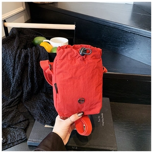 Detailed close-up of a red waterproof nylon crossbody bag with drawstring on wooden steps