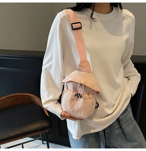 Detail of light pink nylon crossbody bag featuring a drawstring front and adjustable strap
