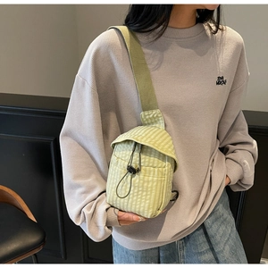 Detail of light green checkered crossbody bag featuring a black bungee cord drawstring closure
