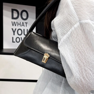 Classic black baguette shoulder bag with gold clasp shown on model with striped shirt