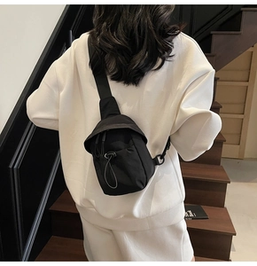 Detail of minimalist black crossbody chest bag with adjustable strap on white sweater