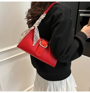 Détail du sac à bandoulière rouge motif crocodile avec boucle dorée et foulard en soie décoratif