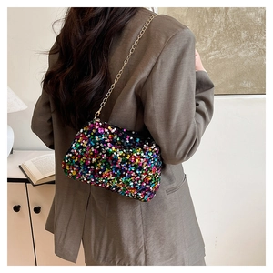 Détail d'un sac à main à paillettes colorées avec chaîne dorée porté sur un blazer gris