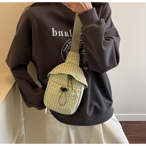 Close-up of light green checkered canvas crossbody bag with drawstring pocket on a model