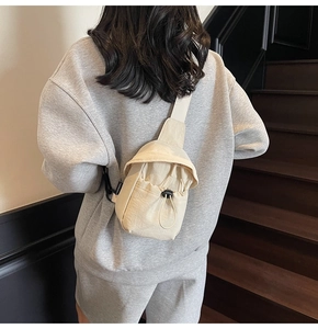 Detail of a beige mini crossbody bag featuring a drawstring closure and black buckle design