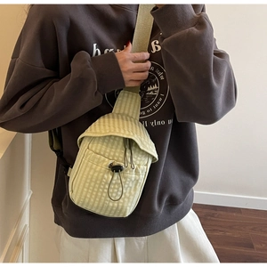 Close-up of light green checkered crossbody bag with drawstring detail and black buckles