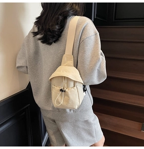 Detail of cream crossbody bag featuring a drawstring front pocket and wide shoulder strap