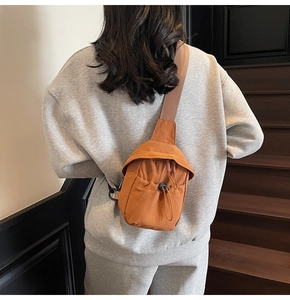 Detail view of the orange canvas crossbody bag showing a drawstring pocket and woven strap