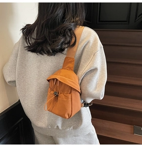Orange canvas crossbody bag featuring drawstring flap closure and wide brown strap