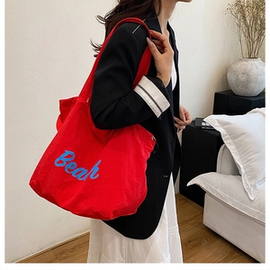 Dettaglio borsa tote in tessuto rosso con stampa Bear blu indossata a spalla in una stanza