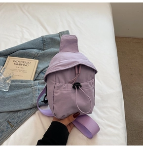 Close-up of a lavender mini crossbody canvas bag featuring a front drawstring pocket on a bed