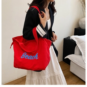 Dettaglio della borsa tote in tela rossa con testo Beach blu e coulisse sulla modella