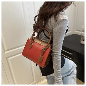 Detail view of brick red and brown two-tone tote bag with gold lettering shown on shoulder