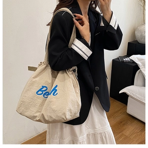 Dettaglio della borsa tote in tela beige con ricamo 'Beh' blu e chiusura a coulisse