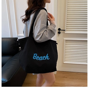 Dettaglio della borsa tote in tela nera con ricamo Beach blu indossata sulla spalla