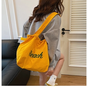 Dettaglio della borsa tote in tela giallo brillante con stampa Beach portata da modella