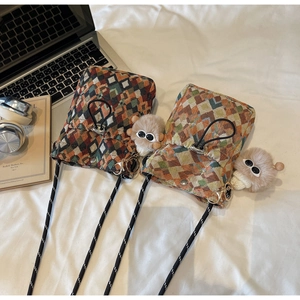 Flat lay of checkered knit crossbody bags with striped straps and plush charms on white desk
