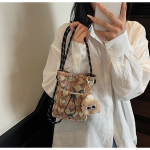 Detail view of colorful geometric woven bag with rope strap and plush charm on model