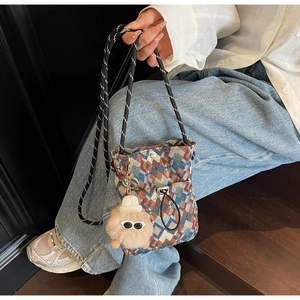 Detail of checkered crossbody phone bag featuring a yellow plush monster keychain