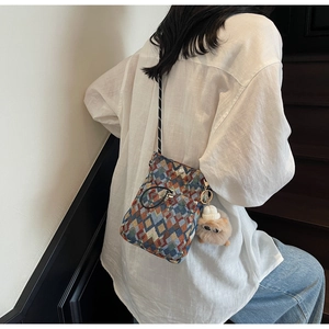 Detail of colorful geometric plaid crossbody bag with a plush monster charm on a model